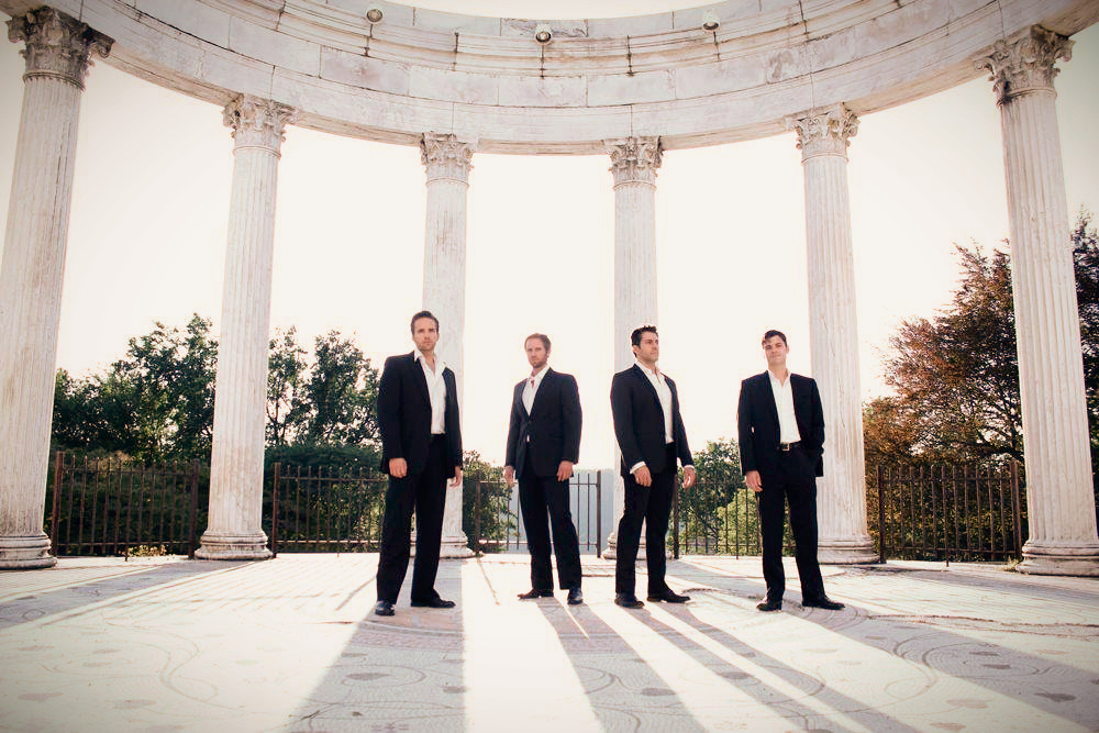 Four men in black suits inside a classical white rotunda with columns