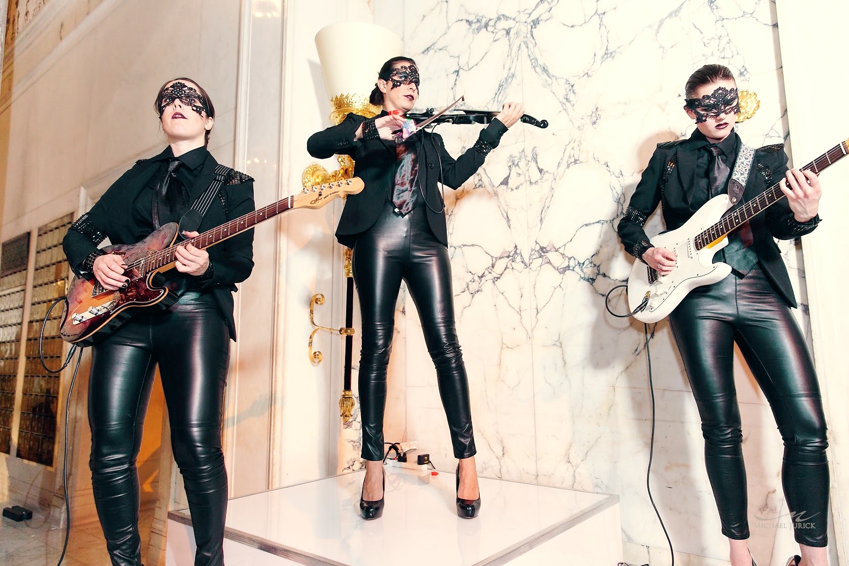 Masked musicians in leather playing guitars and violin in a marble interior