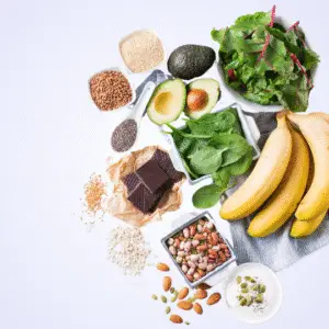 Flat lay of healthy foods including bananas, avocado, leafy greens, nuts and seeds