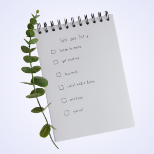 Spiral notebook with a self-care checklist beside a eucalyptus sprig