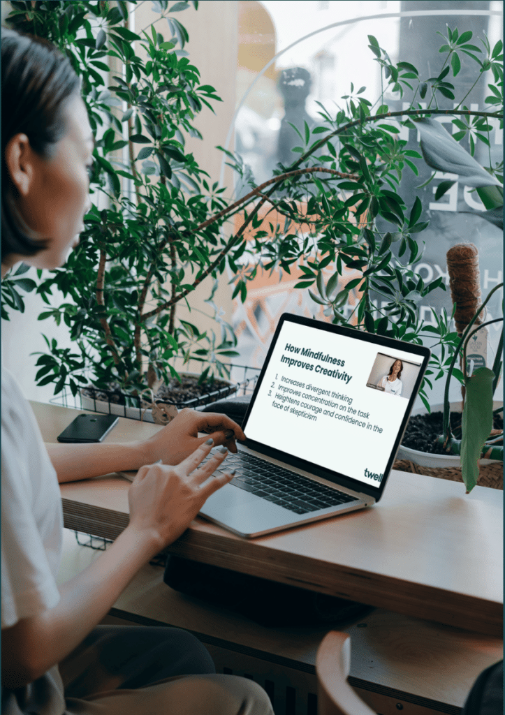 A person watching a Twello class titled How Mindfulness Improves Creativity on a laptop, surrounded by houseplants