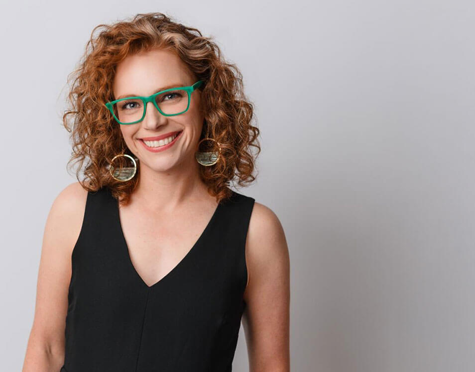 Allie Siegel headshot with green glasses and hoop earrings, smiling