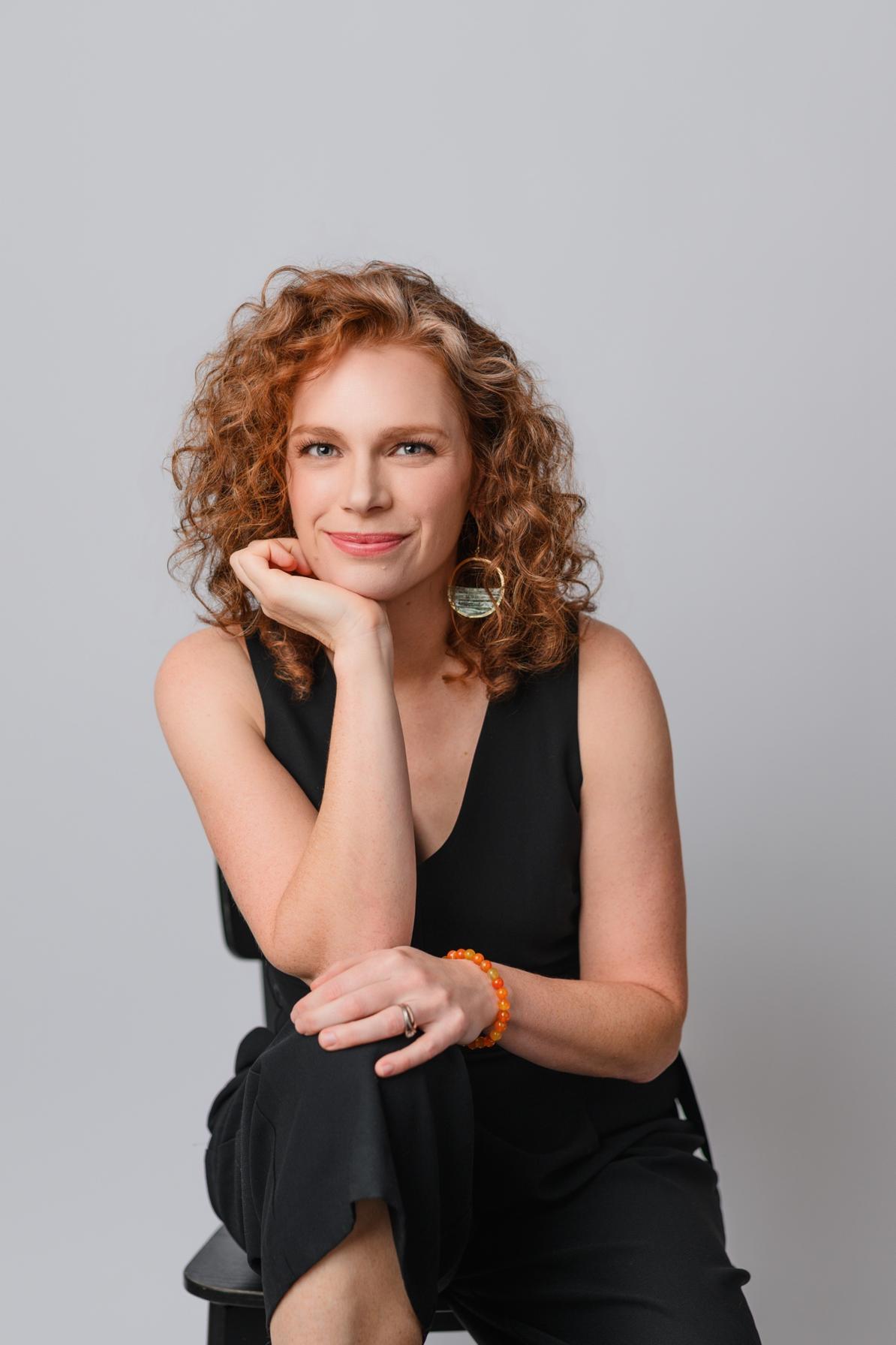Allie Siegel seated on a stool in a black outfit, studio portrait