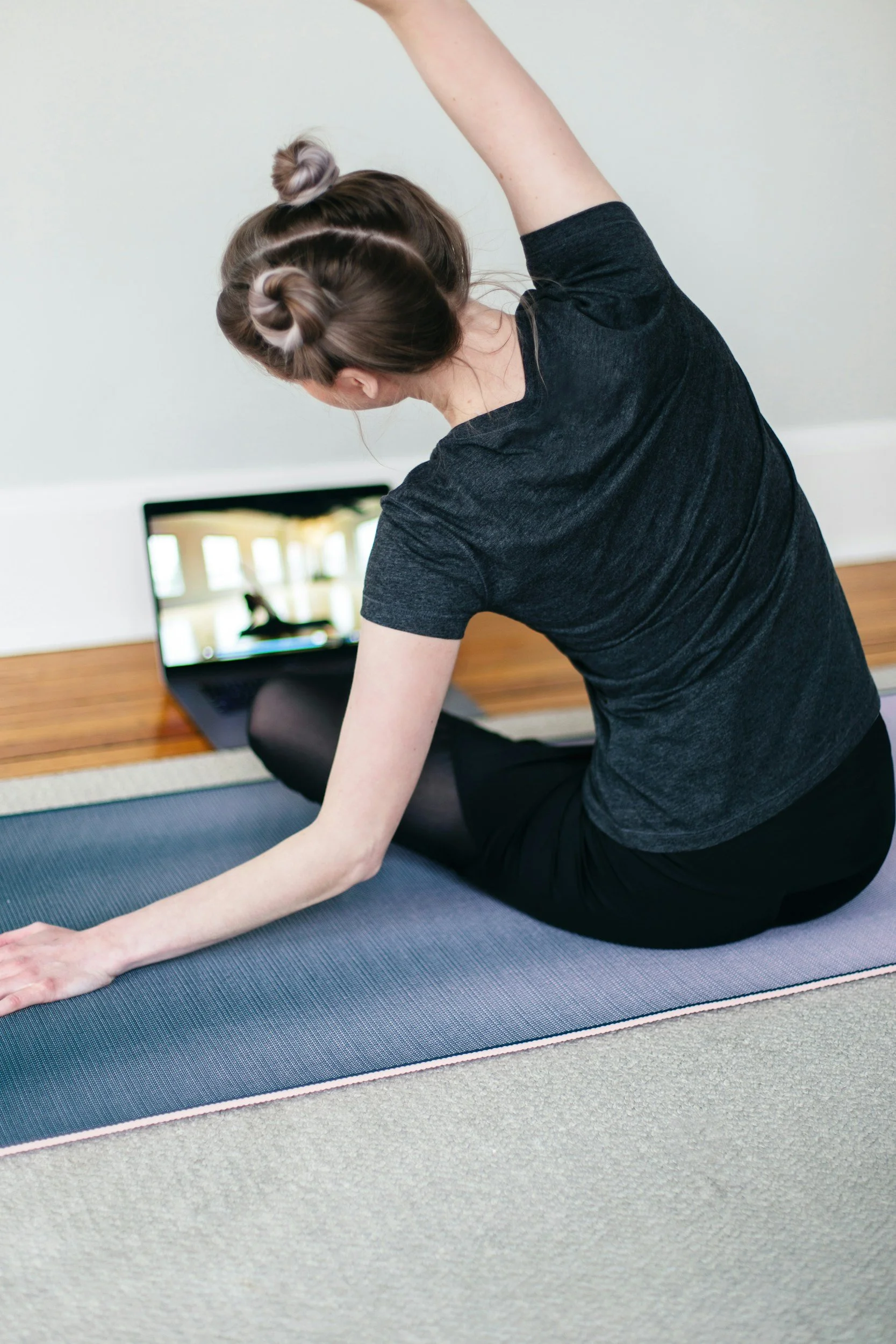 Woman stretching on a yoga mat while watching a fitness video on a laptop