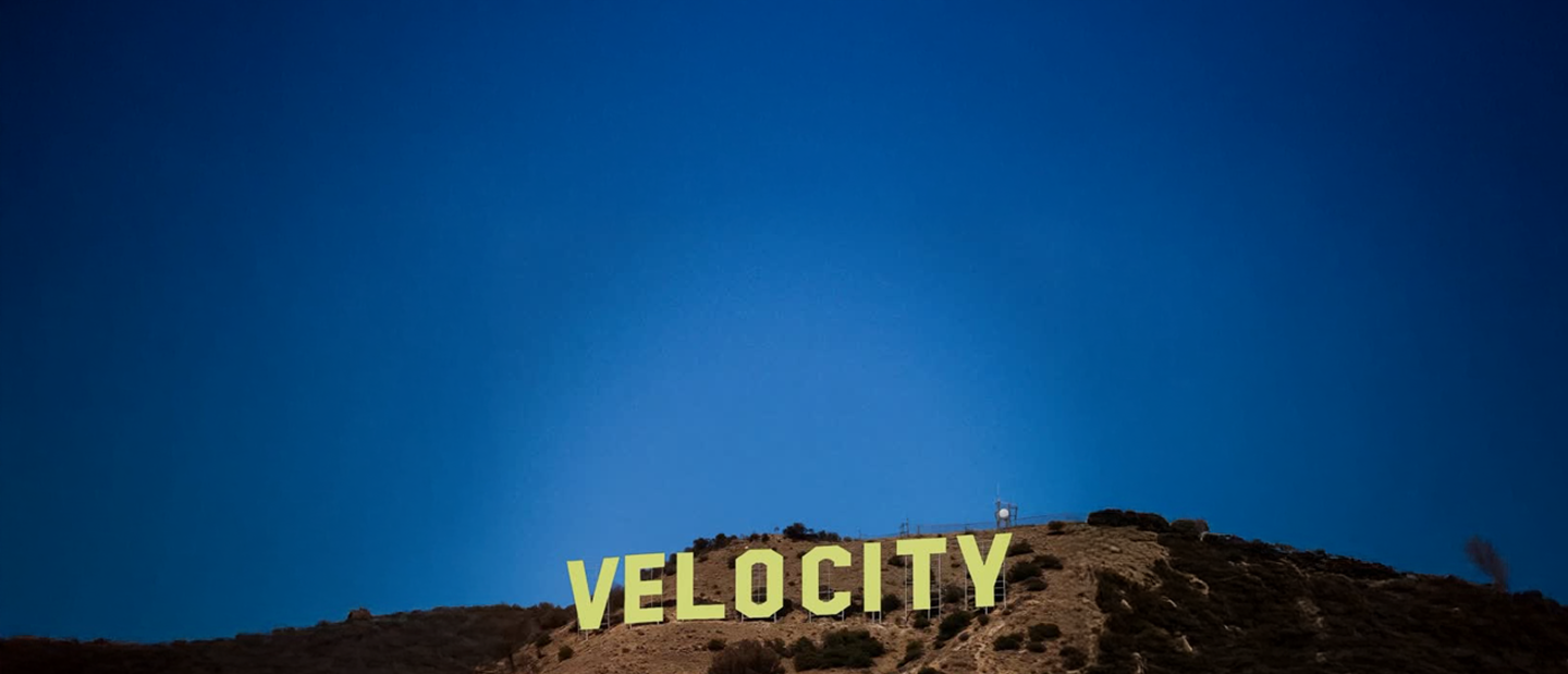 Hillside sign reading VELOCITY in yellow letters against a deep blue sky