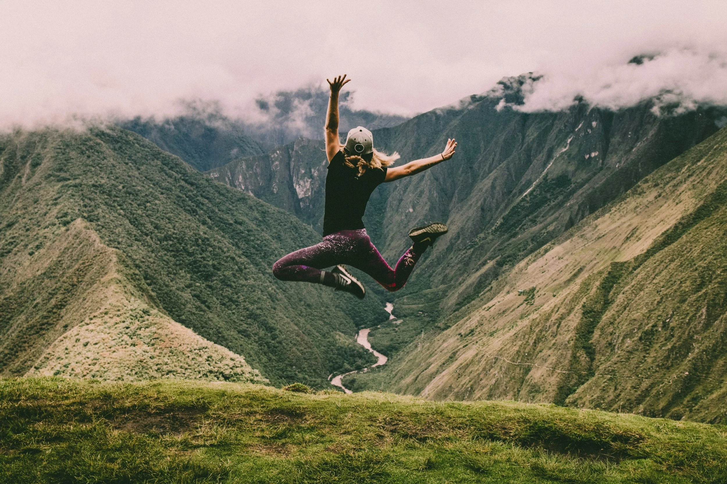 A woman jumping joyfully in mid-air against a dramatic mountain valley