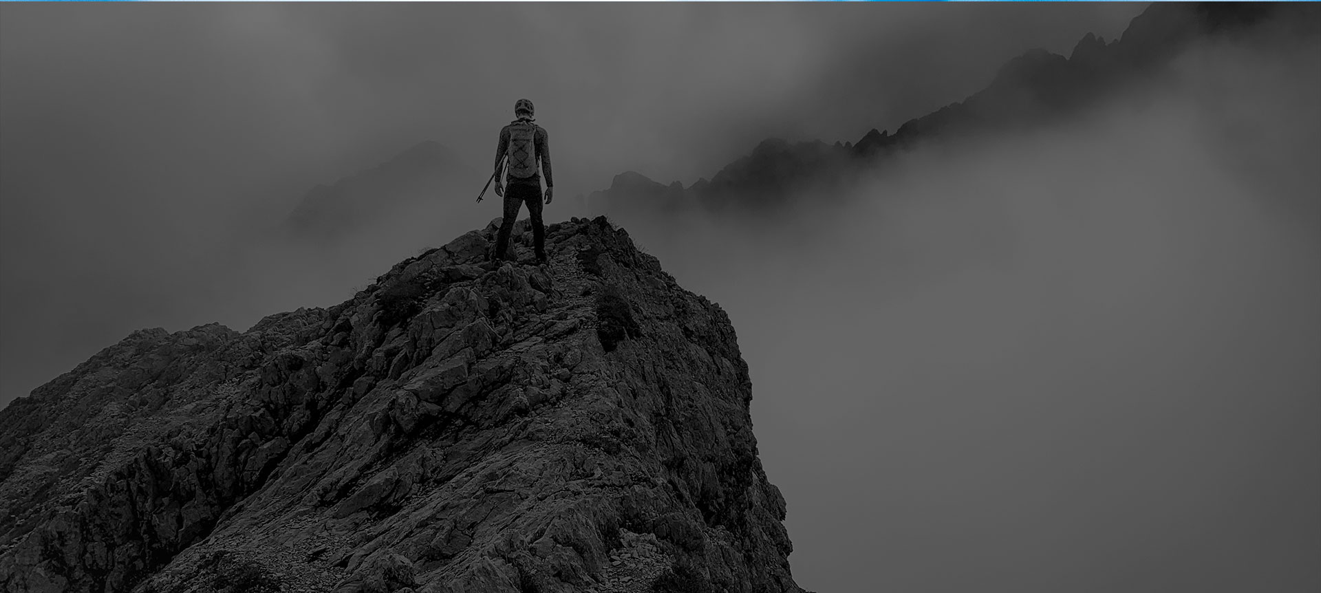 Black-and-white photograph of a hiker standing on a summit in fog