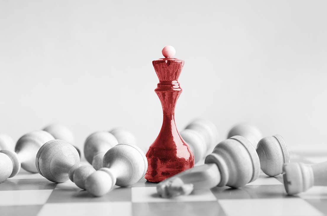 A red chess queen standing among fallen white chess pieces — a metaphor for strategy