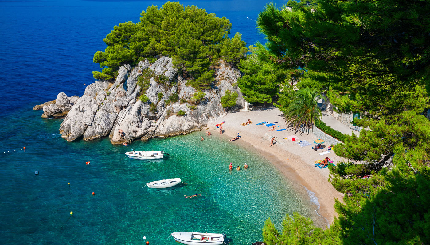 Aerial view of a small Croatian beach cove with turquoise water, pines and small boats