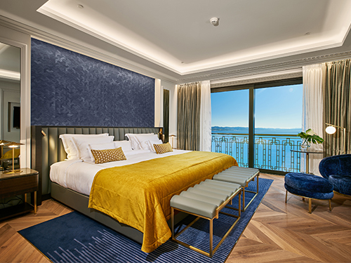 Elegant luxury hotel bedroom with yellow bedspread and a sea-view balcony