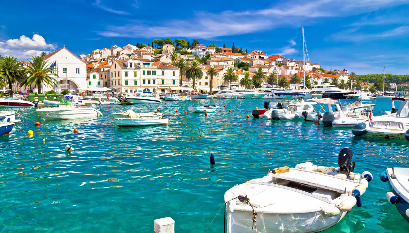 Hvar harbour with white boats moored in turquoise water, old town buildings and palm trees behind