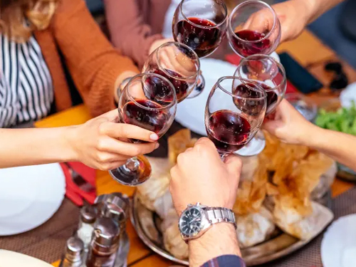 Group toasting with red wine glasses at a restaurant table