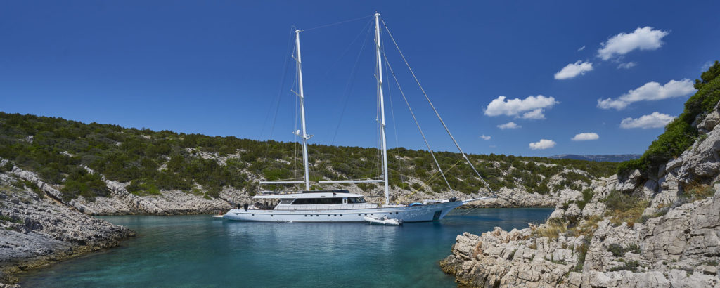 Large white luxury sailing yacht moored in a secluded Croatian bay between rocky cliffs
