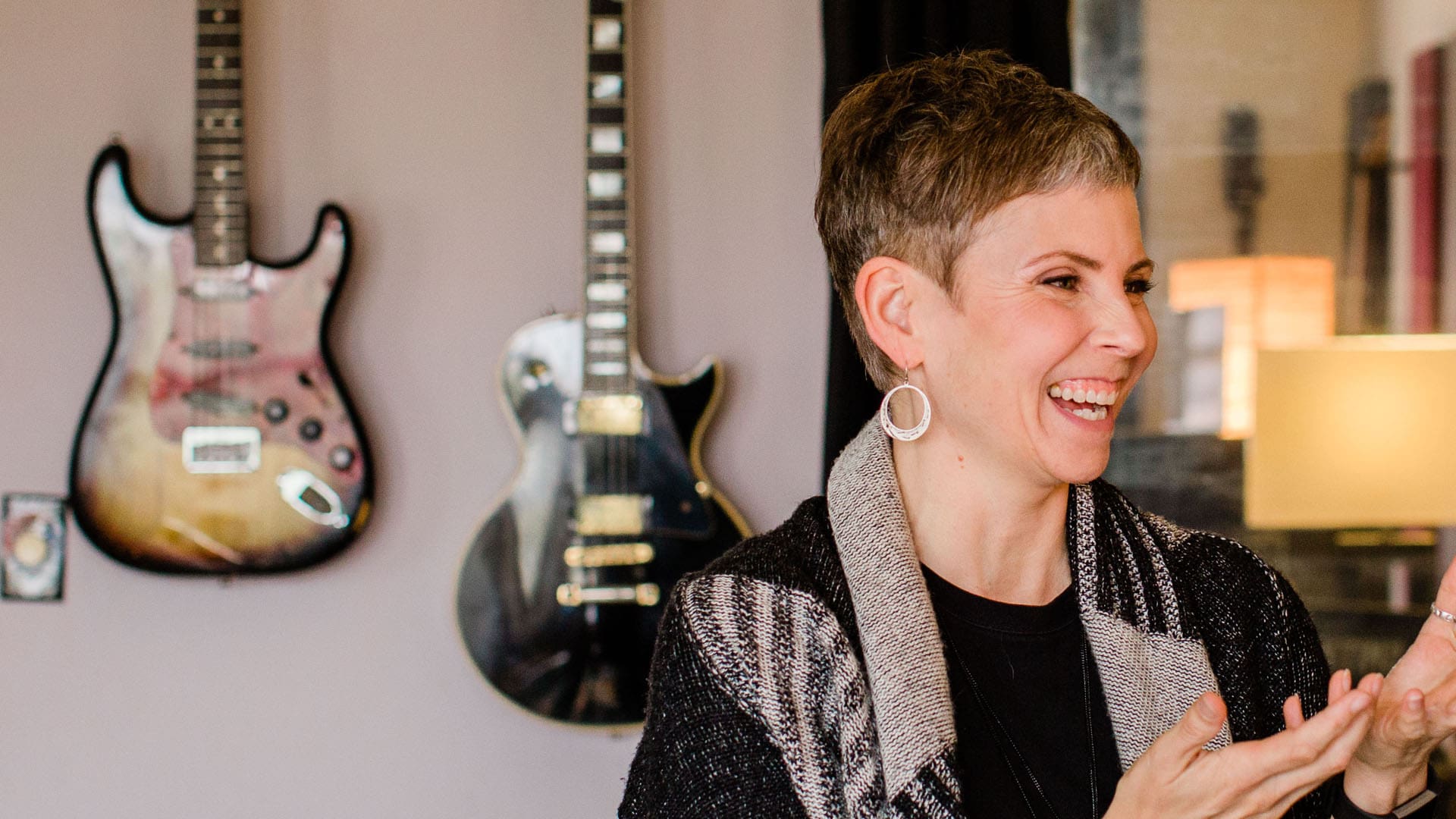 Lauri Smith laughing with two electric guitars mounted on the wall behind her