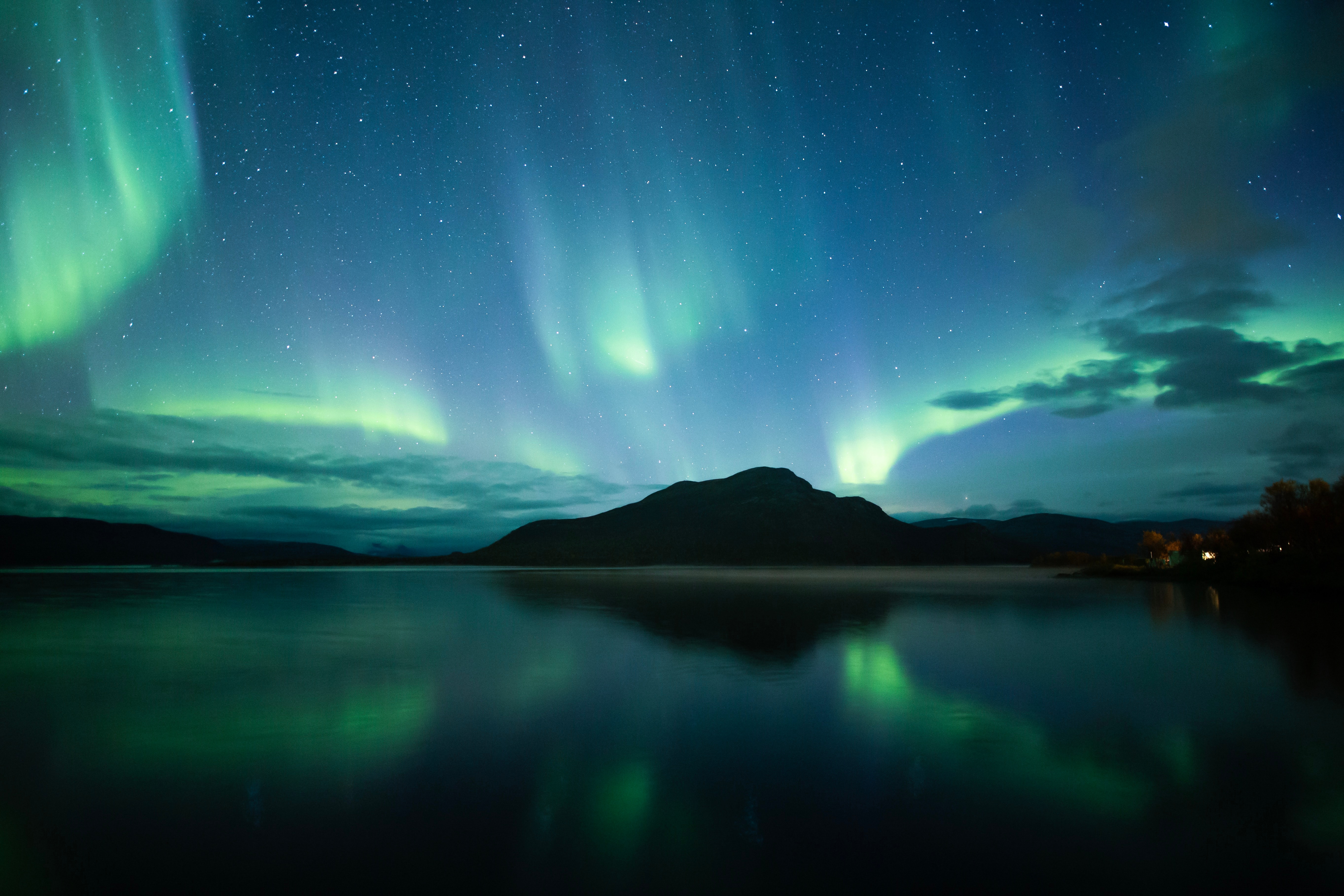 Aurora borealis with vivid green curtains reflected in a calm mountain lake at night