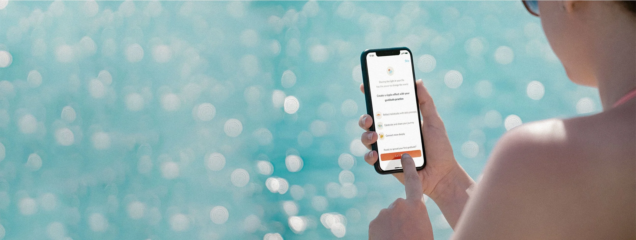 Hand holding an iPhone showing the Waveflow gratitude app, teal water bokeh behind