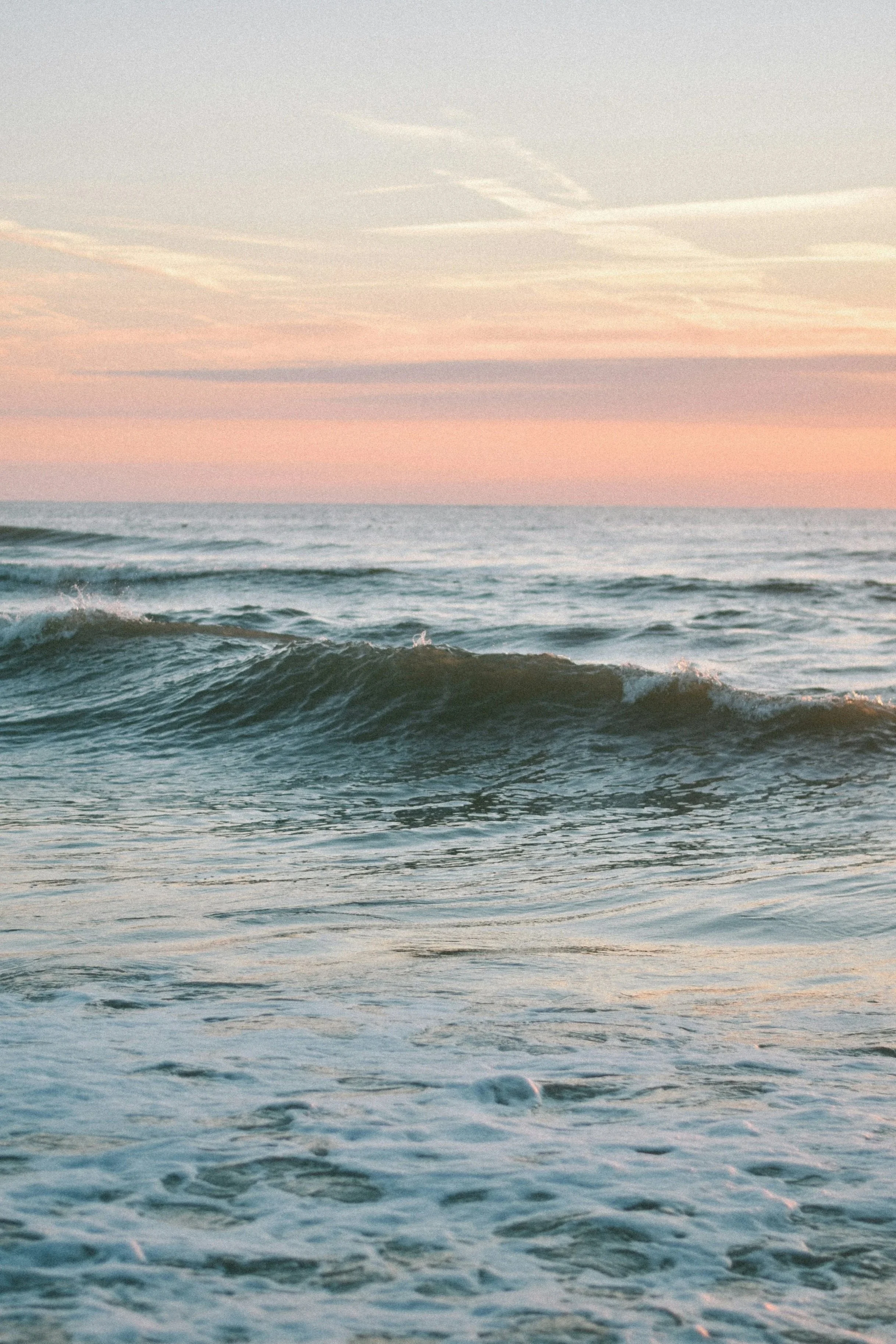 Ocean wave breaking at sunset under a coral pink sky, shot from water level