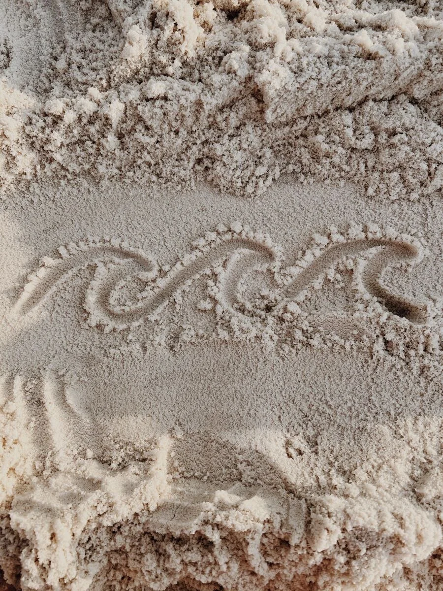 Waveflow wave logo drawn in beach sand — happy friday