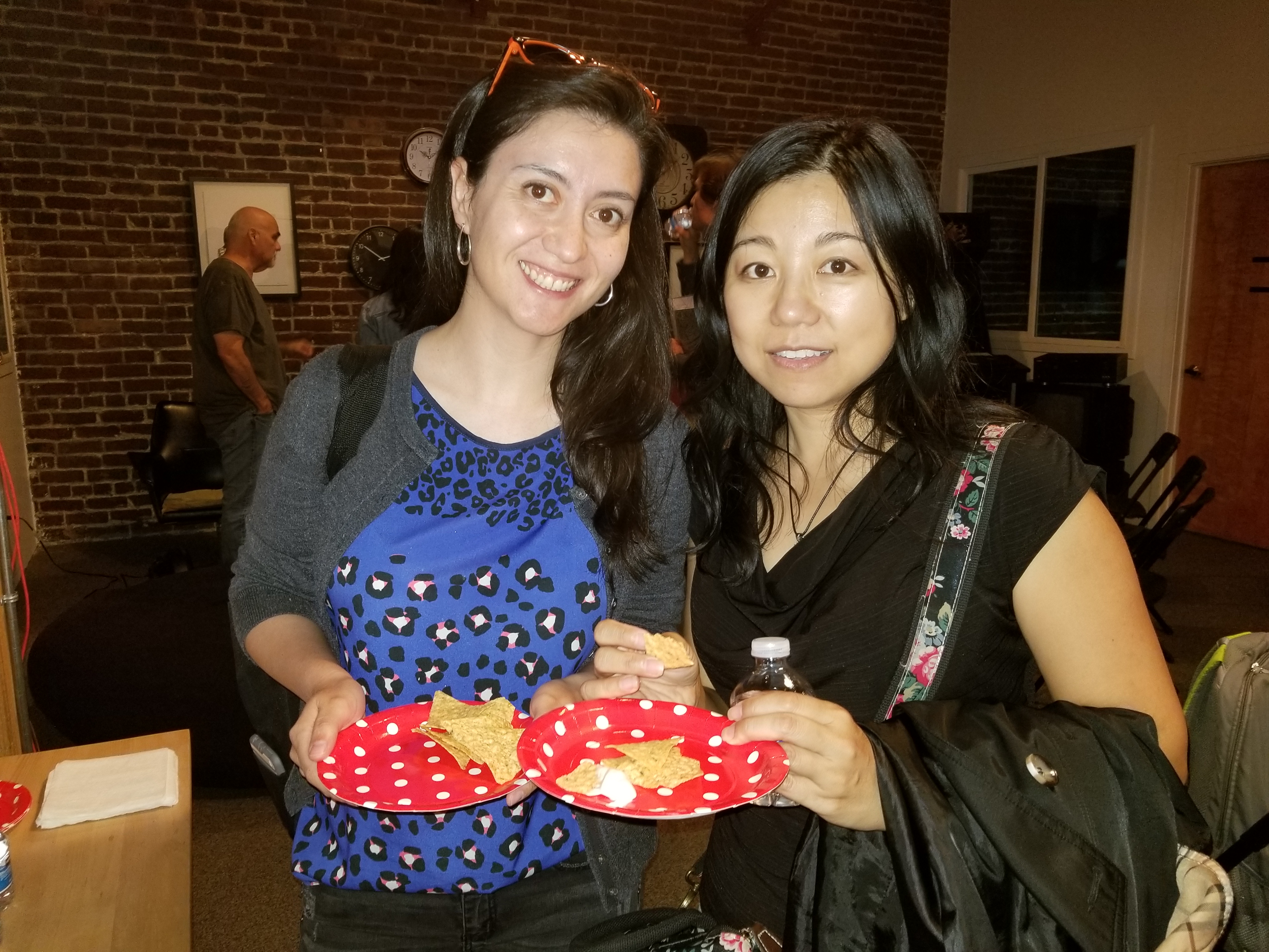 Two attendees smiling with red polka-dot plates of snacks in front of a brick wall