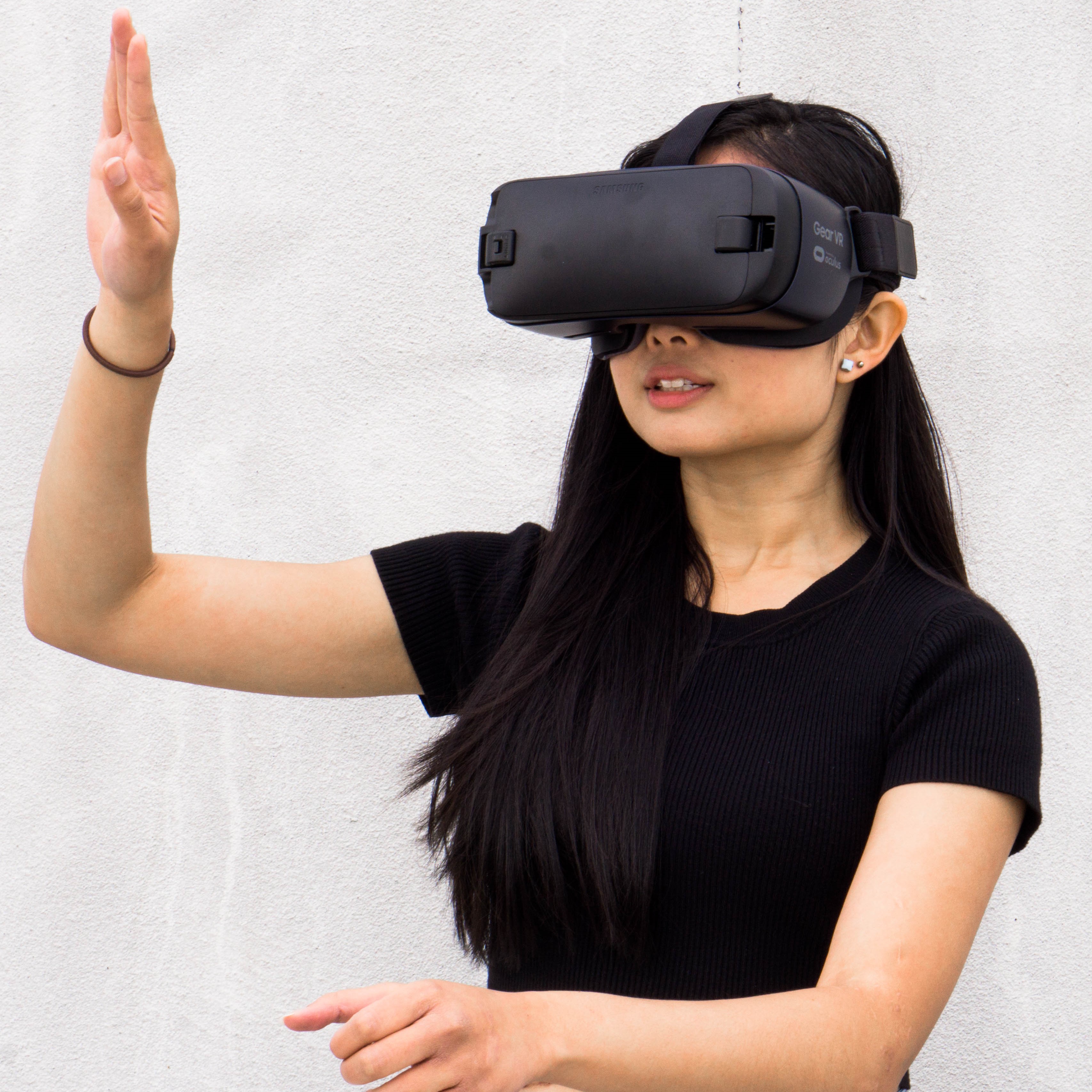 A young woman wearing a Samsung Gear VR headset with her hand raised, testing mixed reality at a WDTnow event