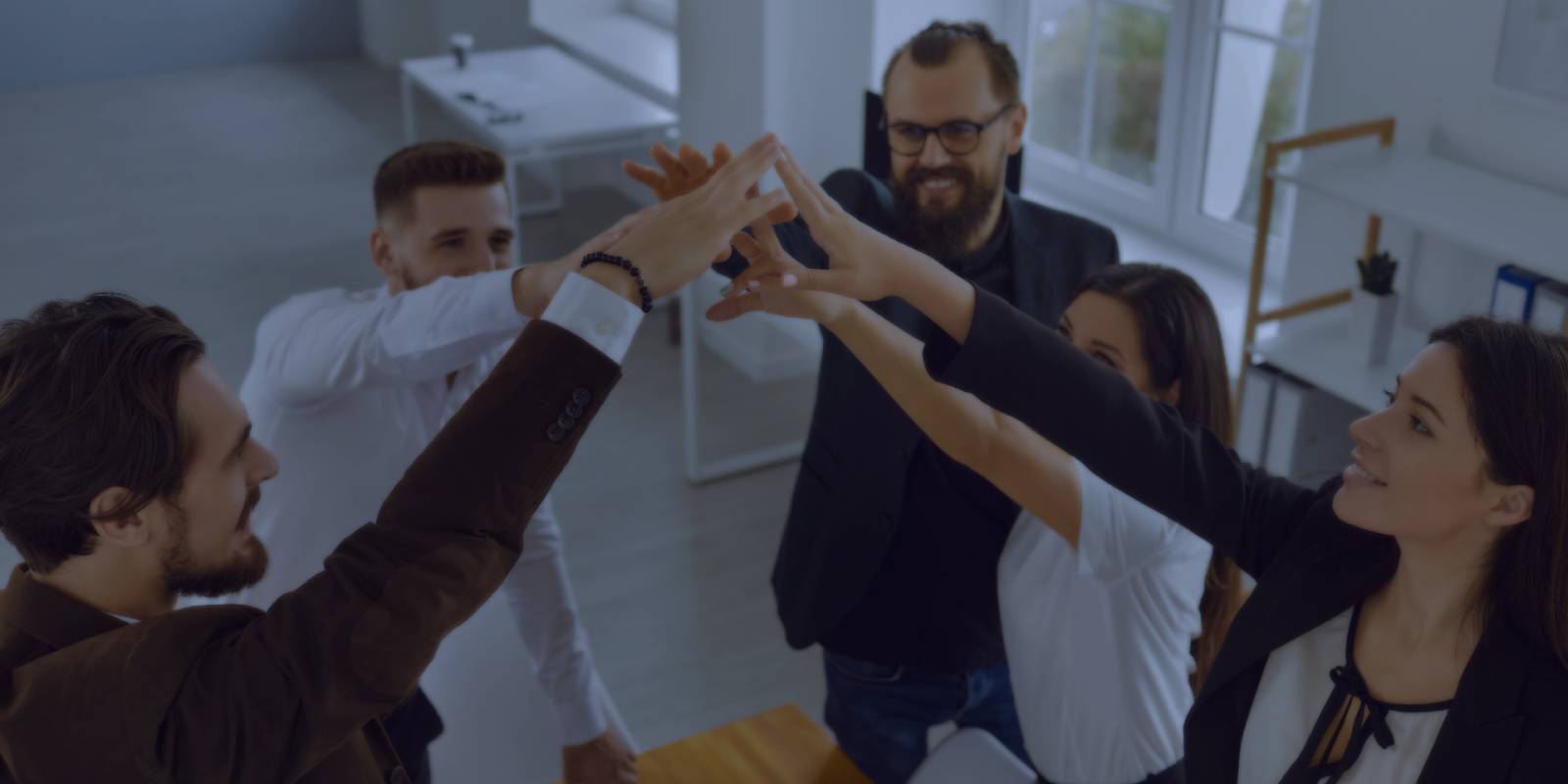 Five business professionals doing a group high-five in a bright office