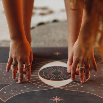 Hands pressing into a dark celestial-patterned yoga mat.
