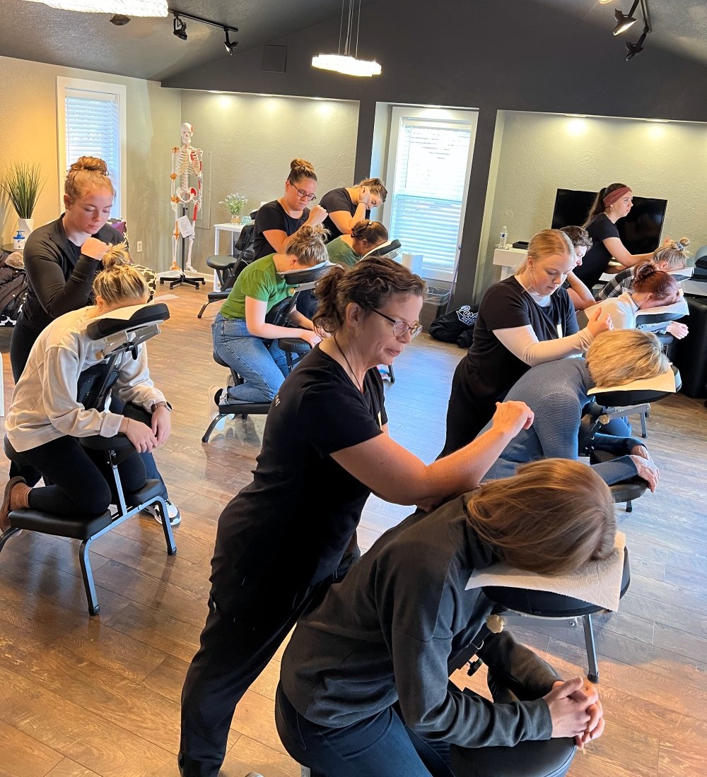 Massage therapy students practicing chair massage on clients in a training room
