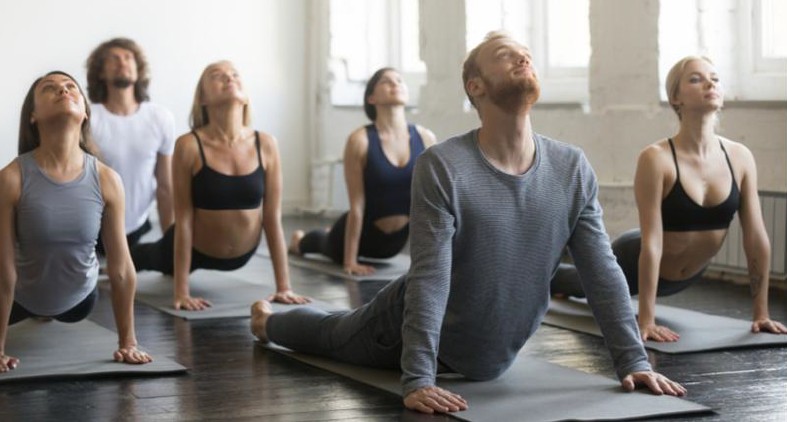 Group of adults performing cobra pose on mats in a bright yoga studio