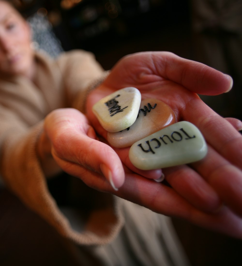 Hands holding three polished stones engraved with words including the word Touch