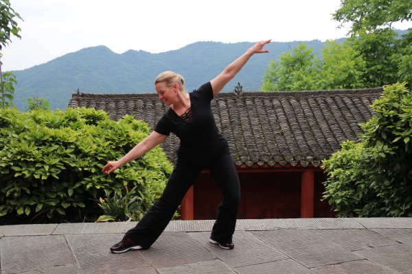 Instructor in black practicing a Tai Chi and qigong pose outdoors in a Chinese garden