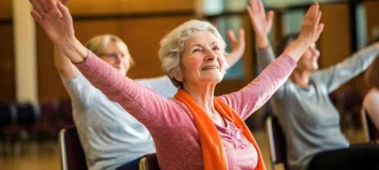 Smiling senior woman with arms raised during a chair and adaptive yoga class
