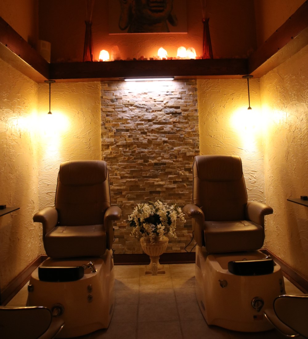 Spa pedicure room with two leather chairs, stone wall and warm amber lighting from Himalayan salt lamps