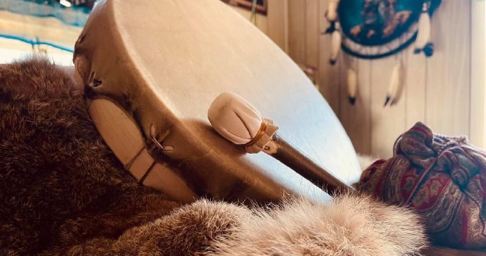 Shamanic drum and beater resting on fur with a dreamcatcher in the background