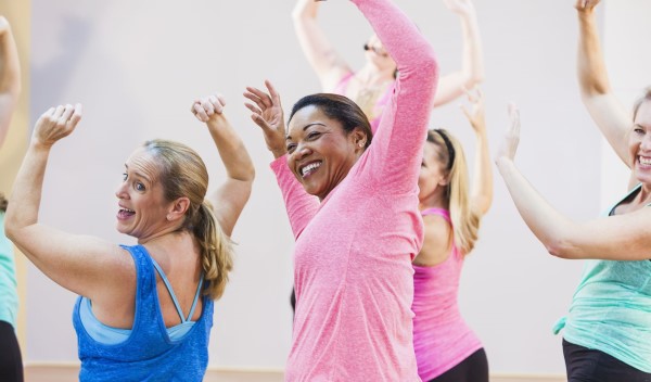 Group of women smiling and dancing with arms raised in a movement class