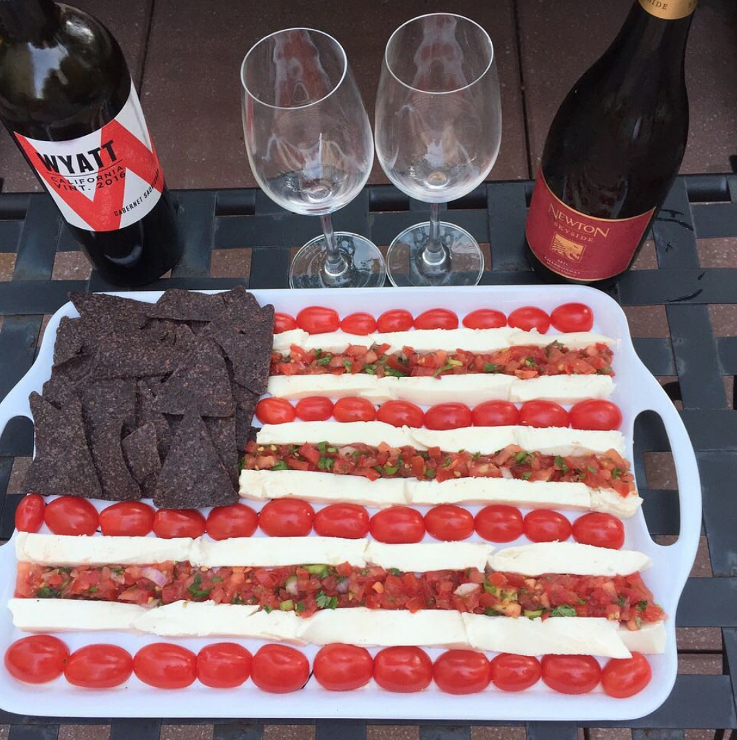American flag charcuterie board of tomatoes, cheese and salsa with two wine bottles