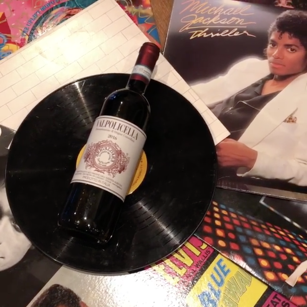 Valpolicella wine bottle resting on a vinyl record beside album covers