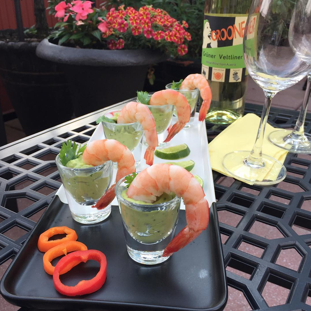 Shrimp cocktail shots on a black tray outdoors with a bottle of Gruner Veltliner