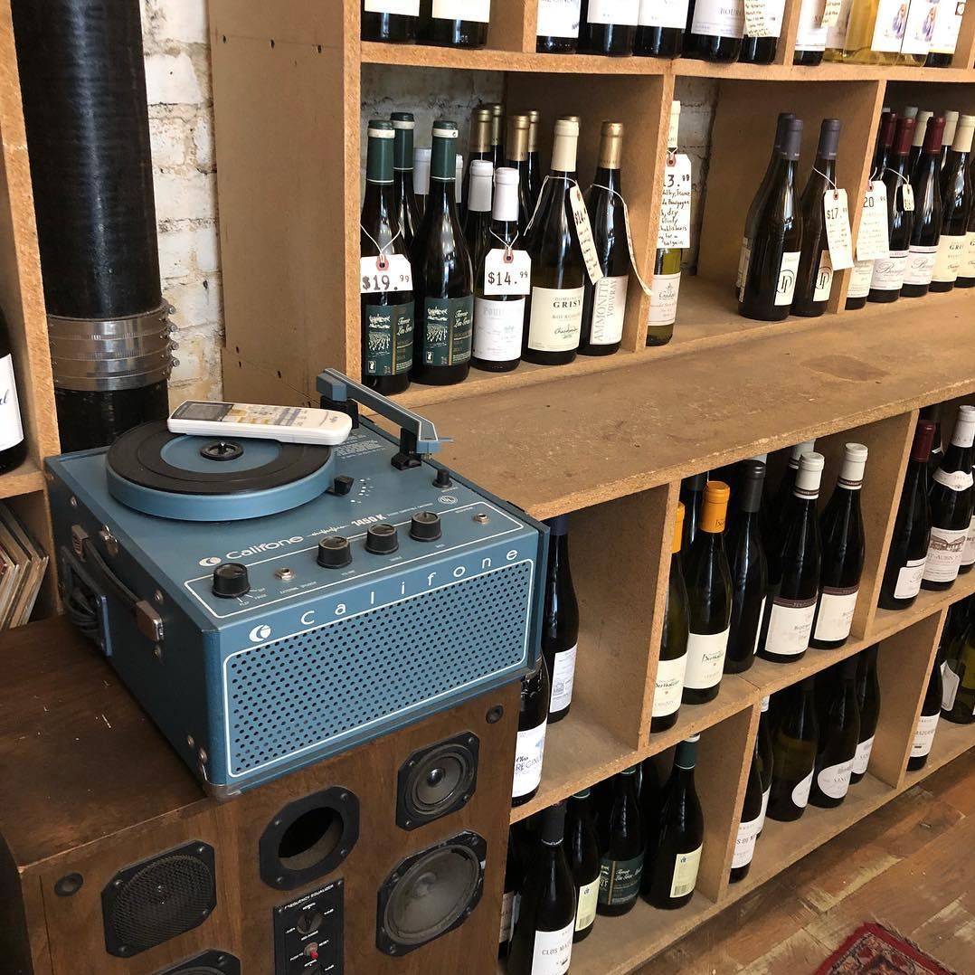 Vintage Califone record player on speakers beside wine shop shelves