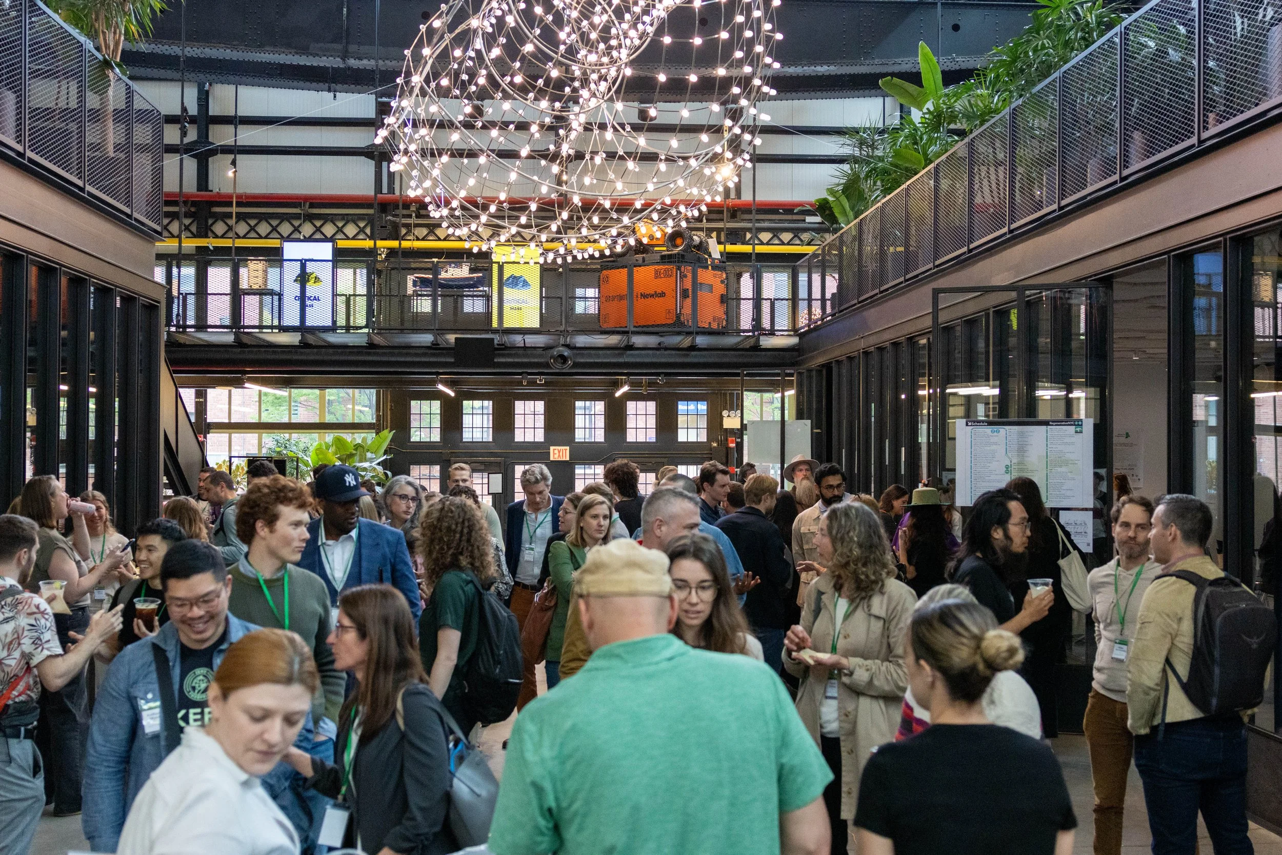 A large crowd of attendees networking inside an industrial atrium venue with string lights at a Why Regenerative event