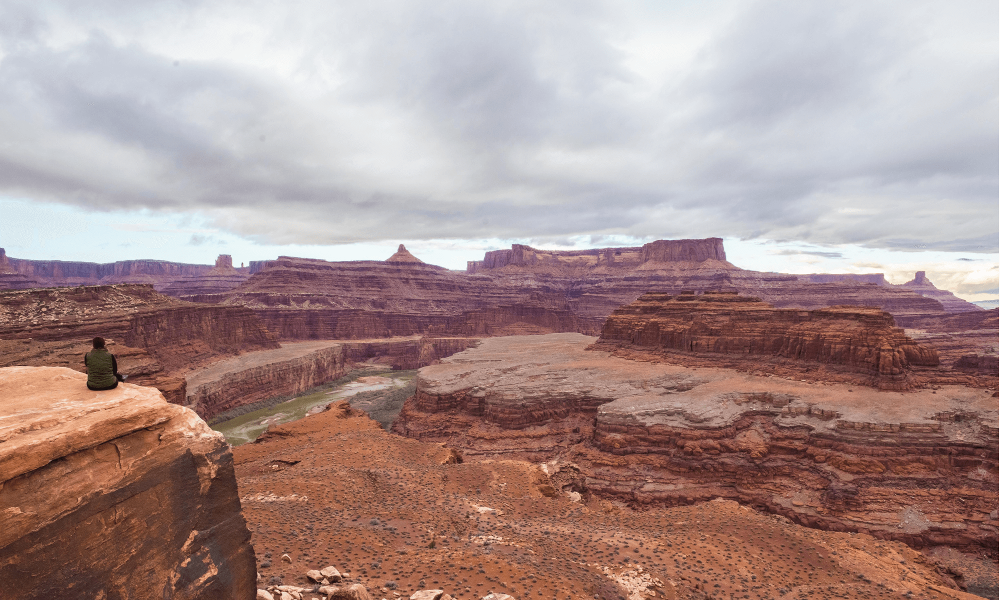 A lone figure sitting on a cliff edge overlooking Canyonlands National Park