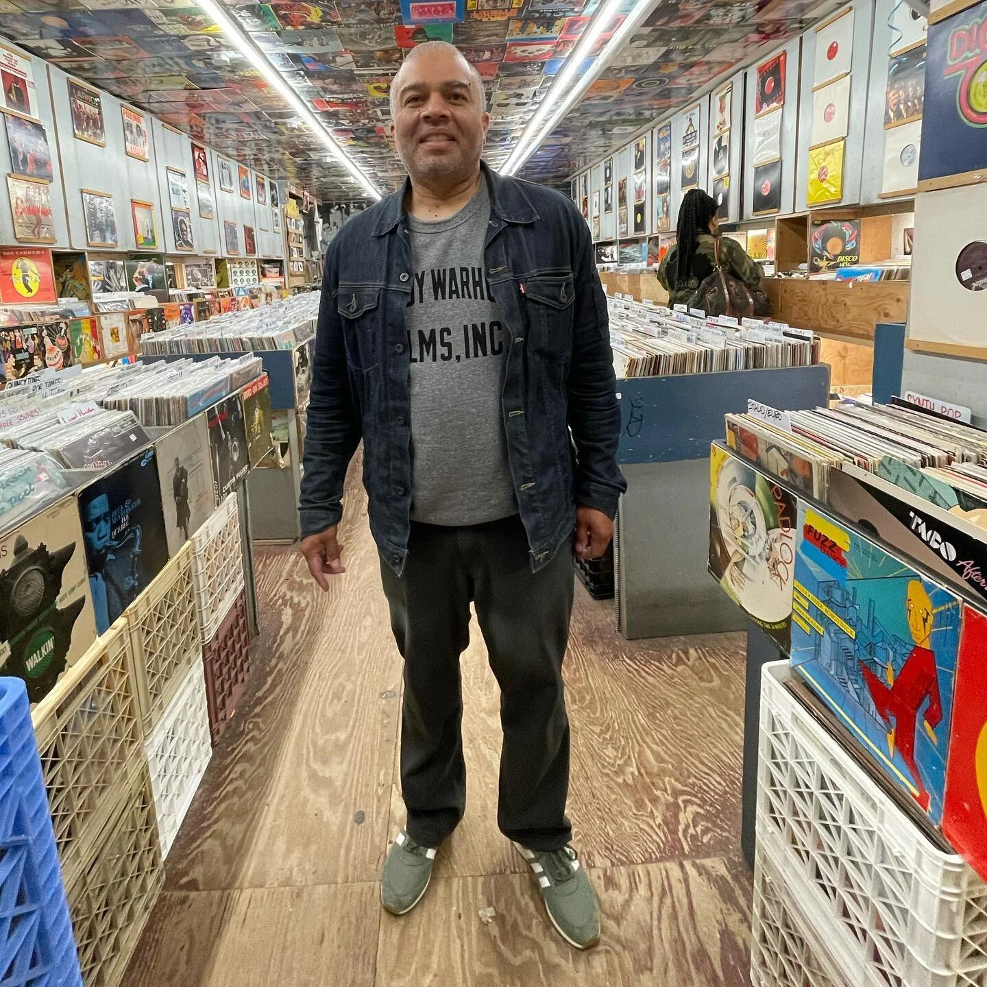 Man in a denim jacket and Andy Warhol Films Inc. t-shirt standing in the record shop aisle