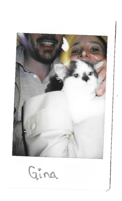 Polaroid of Gina, a small black-and-white kitten held by two smiling people.