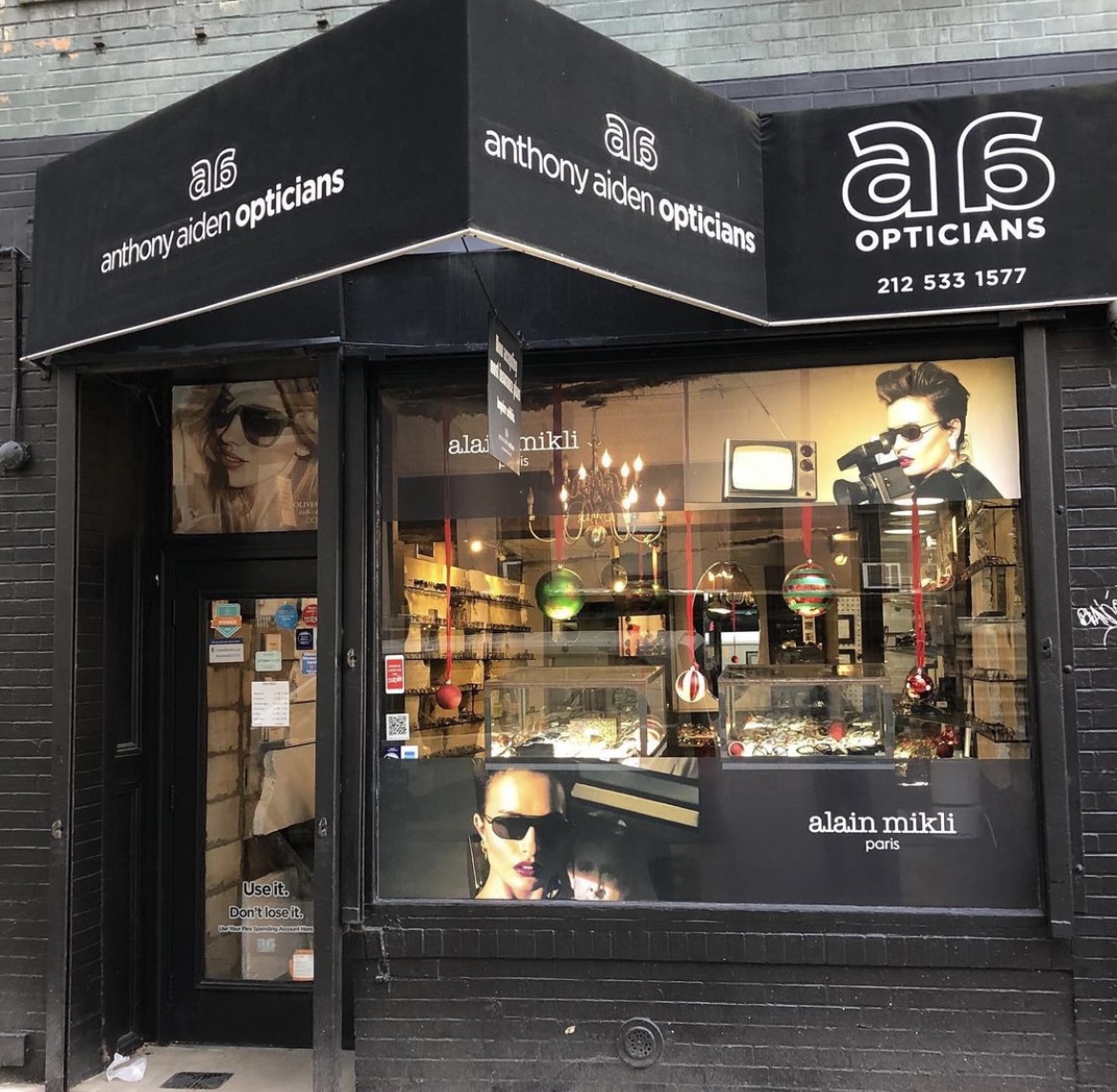 The black-awning storefront of Anthony Aiden Opticians at 42 St. Marks Place, East Village, with frames lit in the window