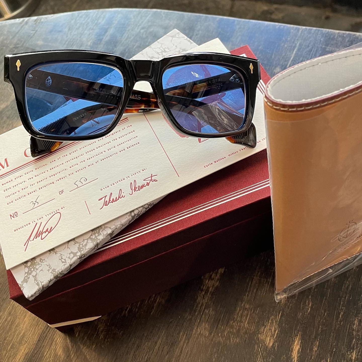 Blue-lens sunglasses resting on a red Jacques Marie Mage box