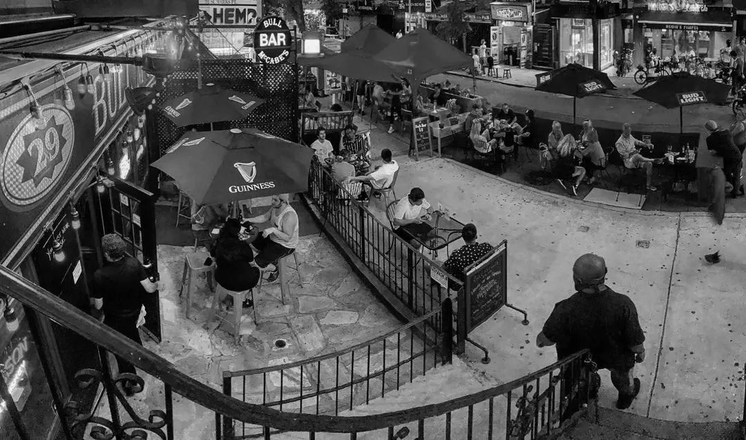 Overhead night-time view of Bull McCabes' outdoor patio seating on St. Mark's Place, patrons under Guinness and Bud Light umbrellas