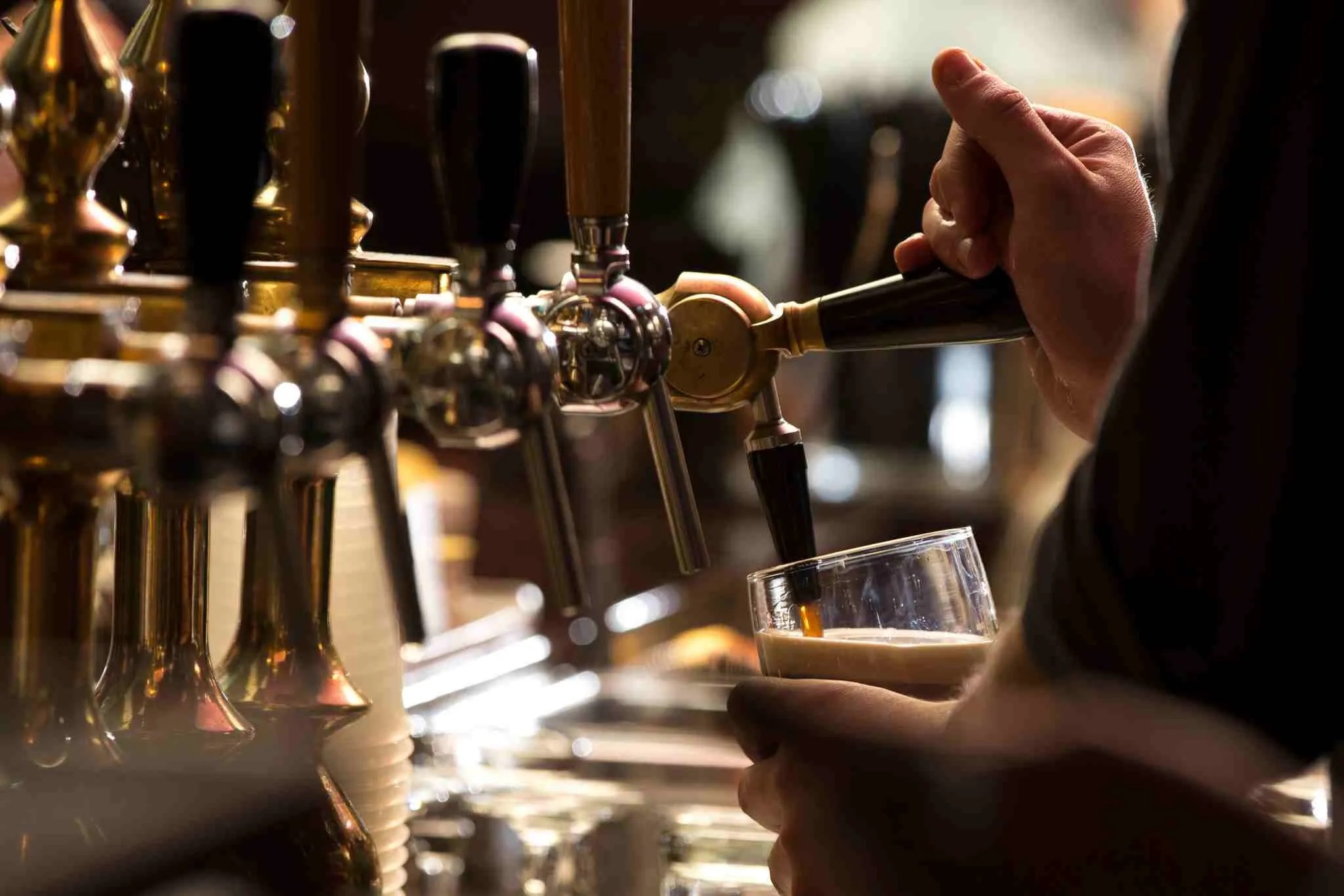 A bartender pouring a pint from brass beer taps in the dimly lit bar at Bull McCabes
