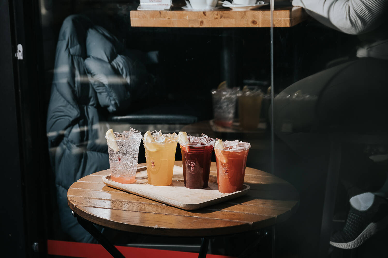 Four iced drinks in Charlotte Cafe branded cups on a wooden tray at a cafe table