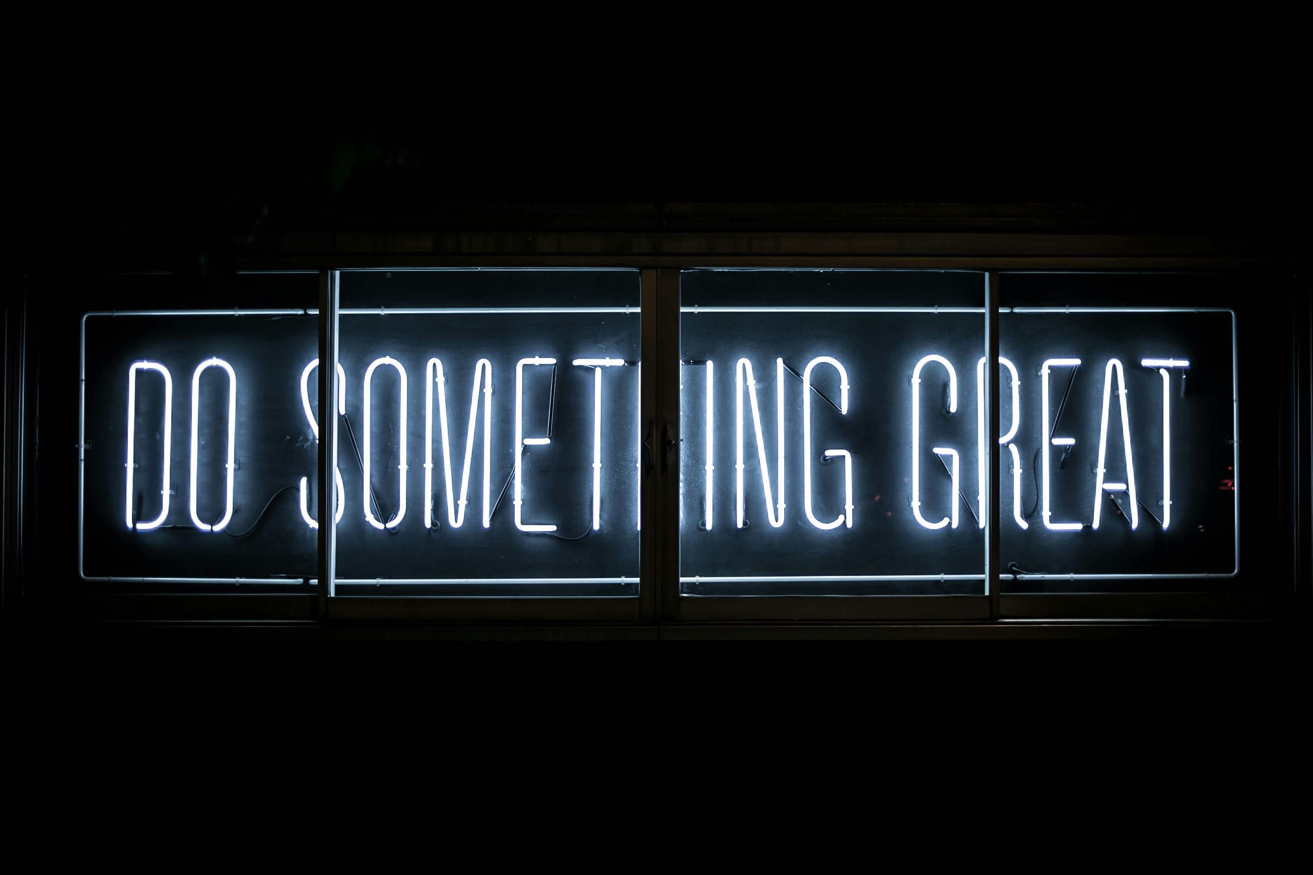 White neon sign in a dark window reading DO SOMETHING GREAT