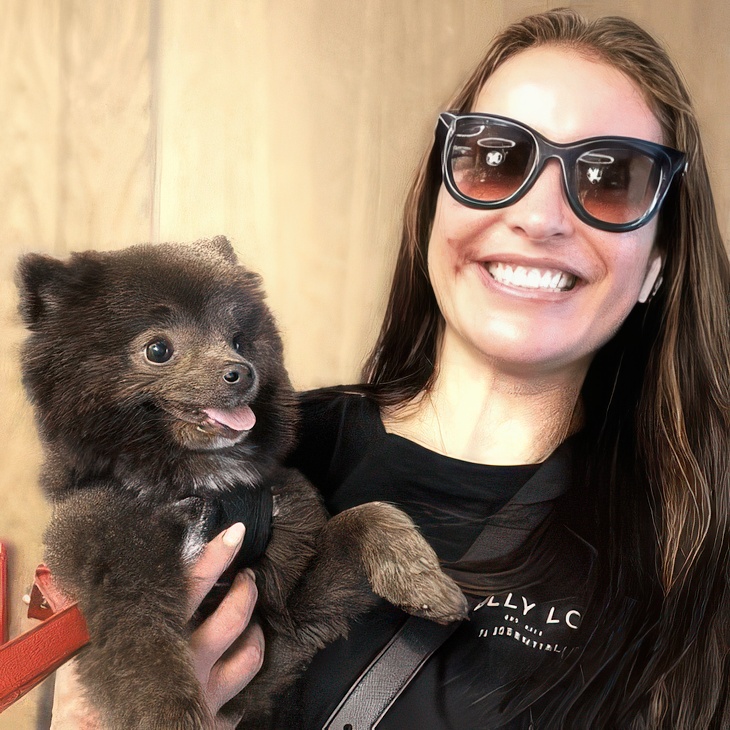 Woman in sunglasses holding a dark brown Pomeranian at DOGMA