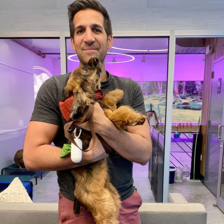 Smiling man holding a small brown wire-haired terrier mix in the DOGMA lobby